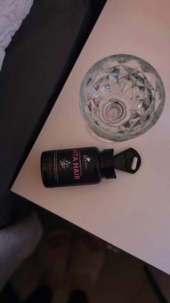 Pote do Vita Hair aberto sobre a mesa, com uma cápsula e um copo ao lado.